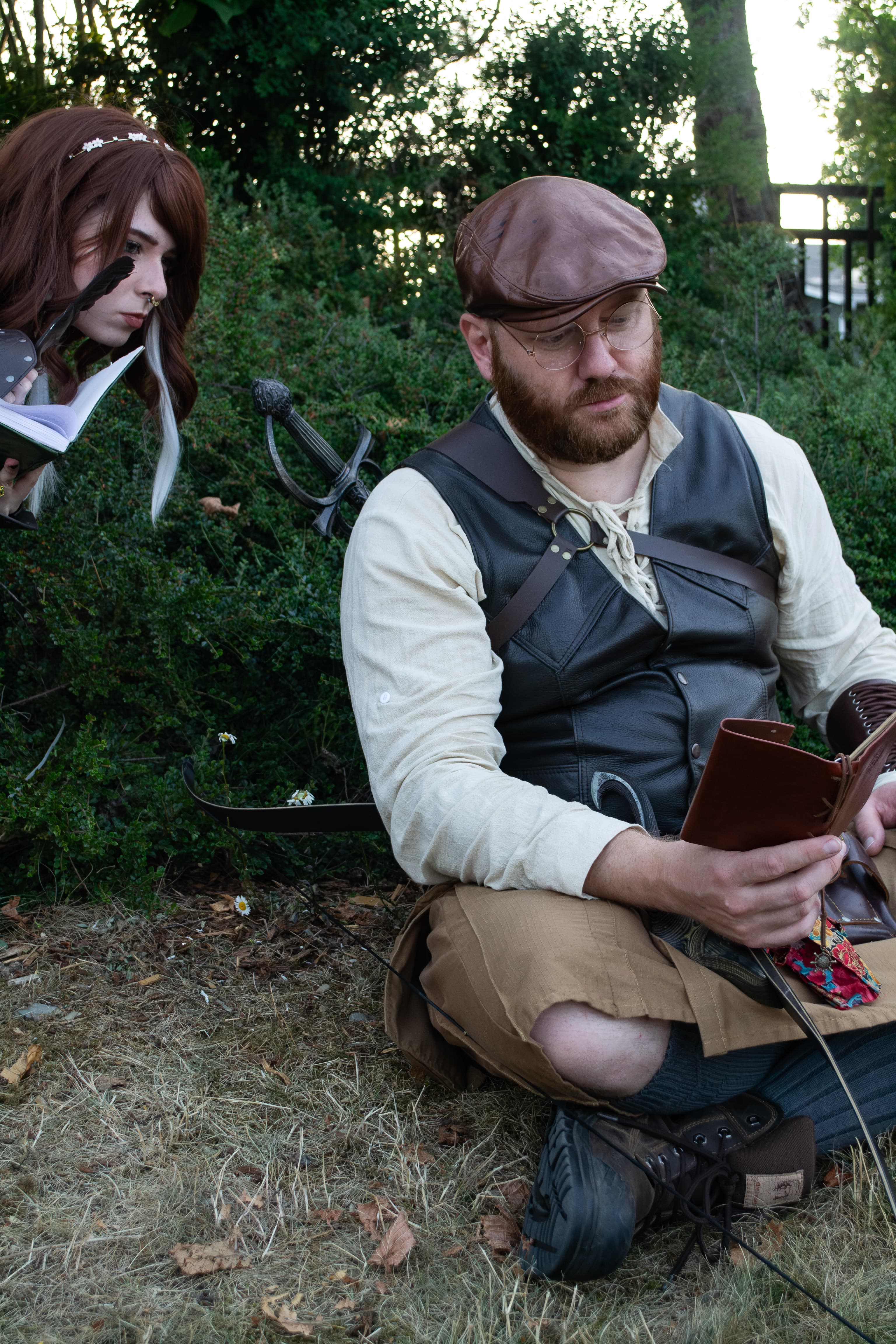 Two people wearing fantasy costumes. One person is reading and the other person is peeking over their shoulder.