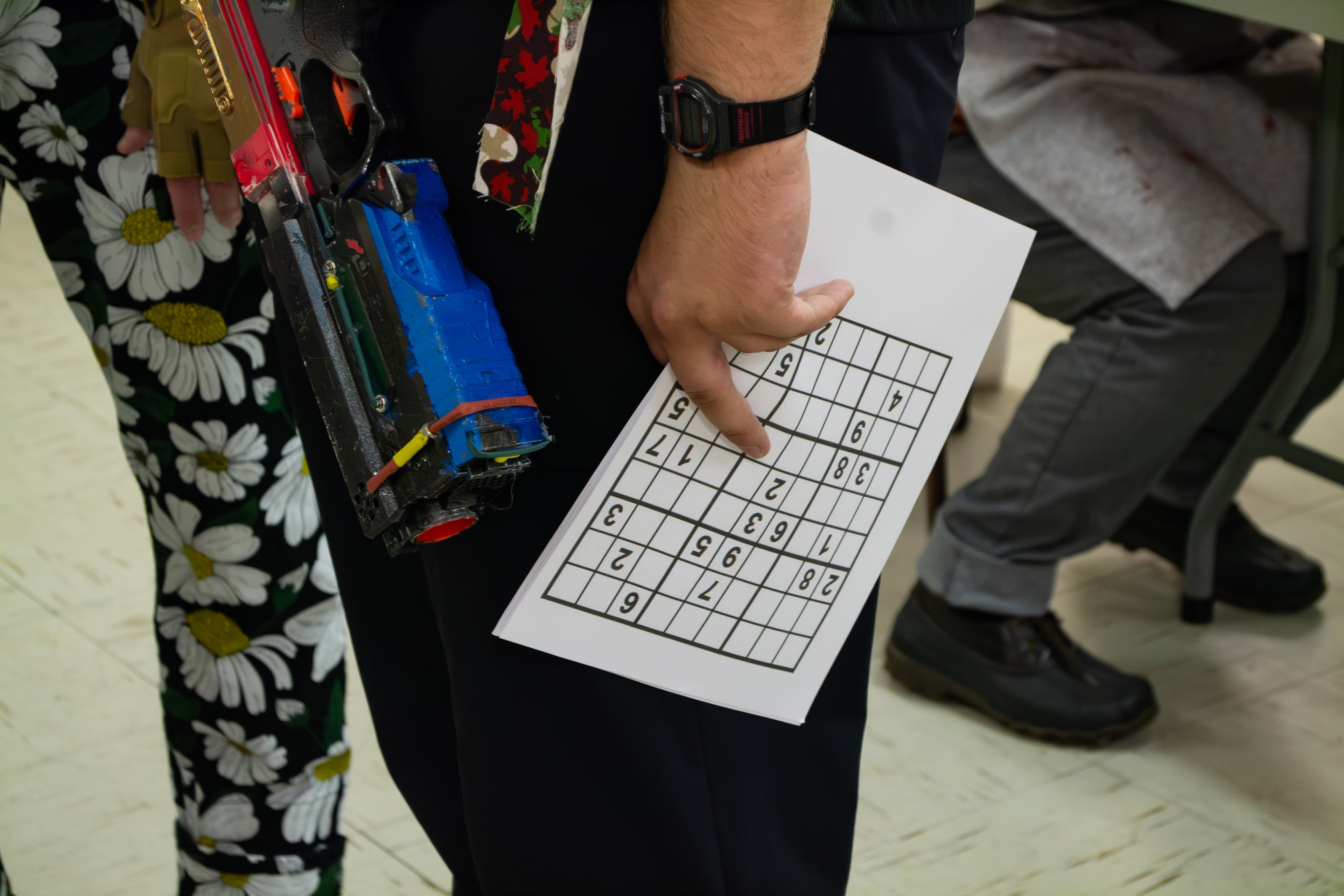 A person holding a plastic prop gun and an unfilled sudoku sheet.