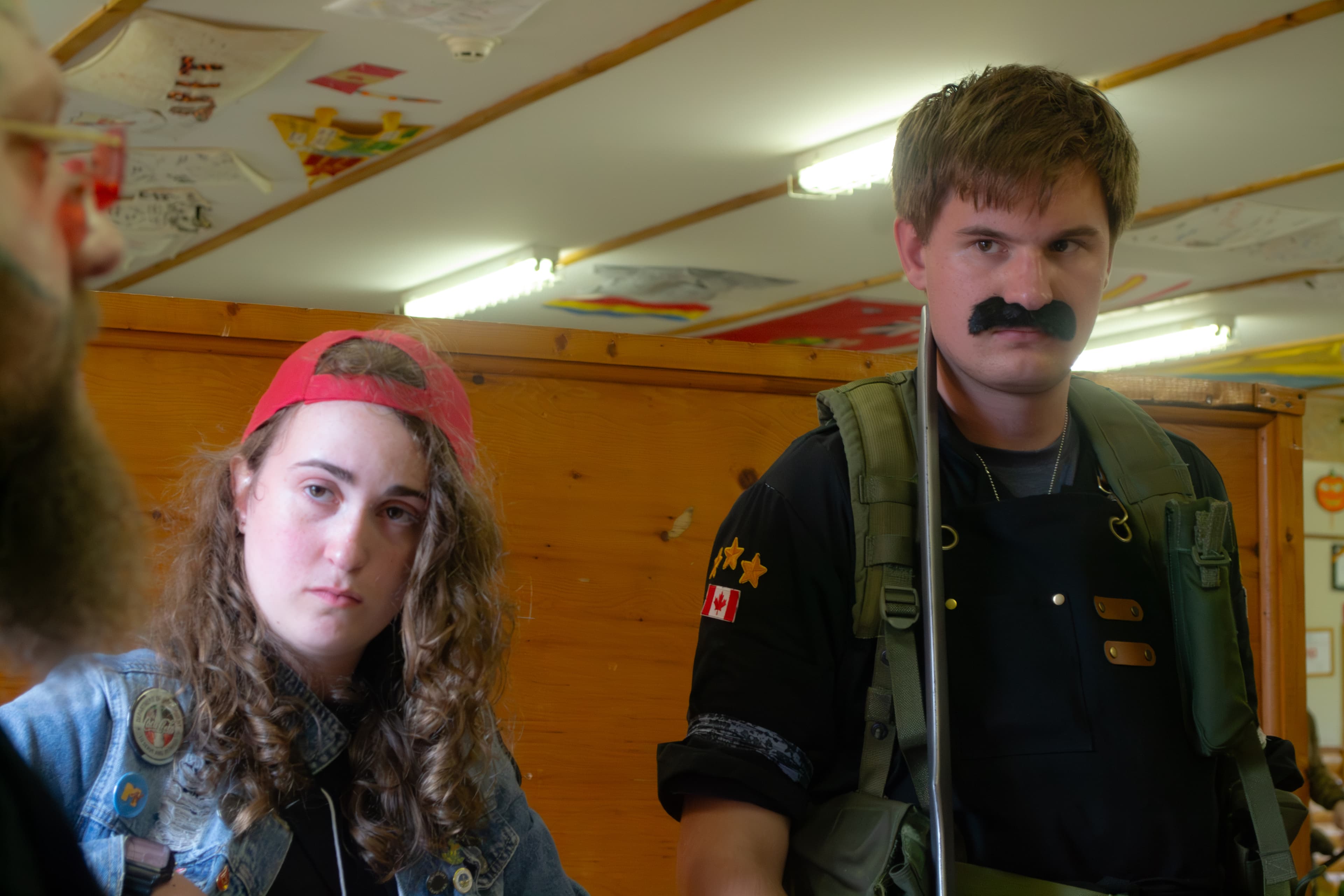 A person wearing an 80's-style vintage outfit and a person wearing a military uniform costume look at a third person who is only partially in the frame.
