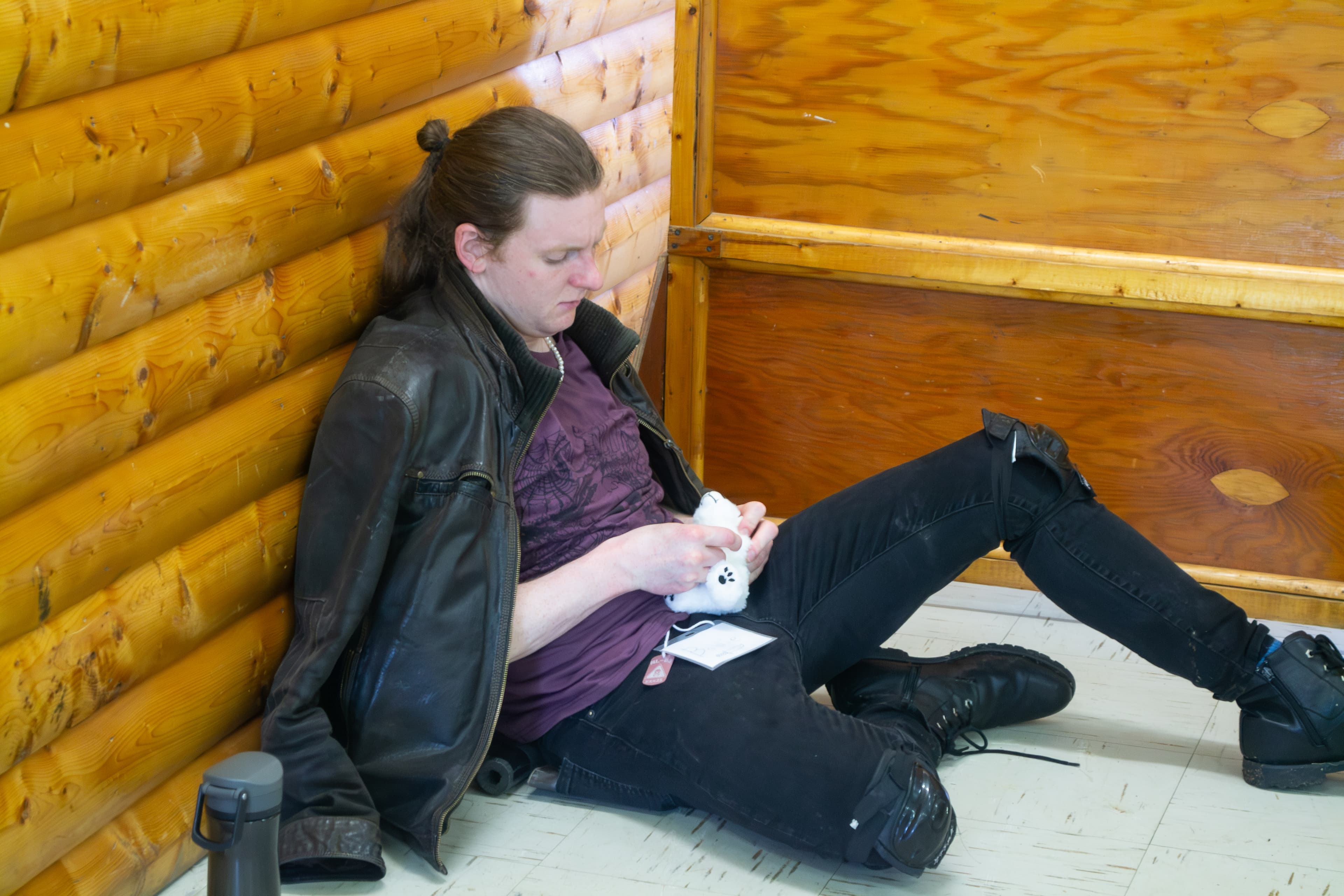A person wearing a post-apocalyptic costume sitting on the floor and stitching up a small polar bear plushie.