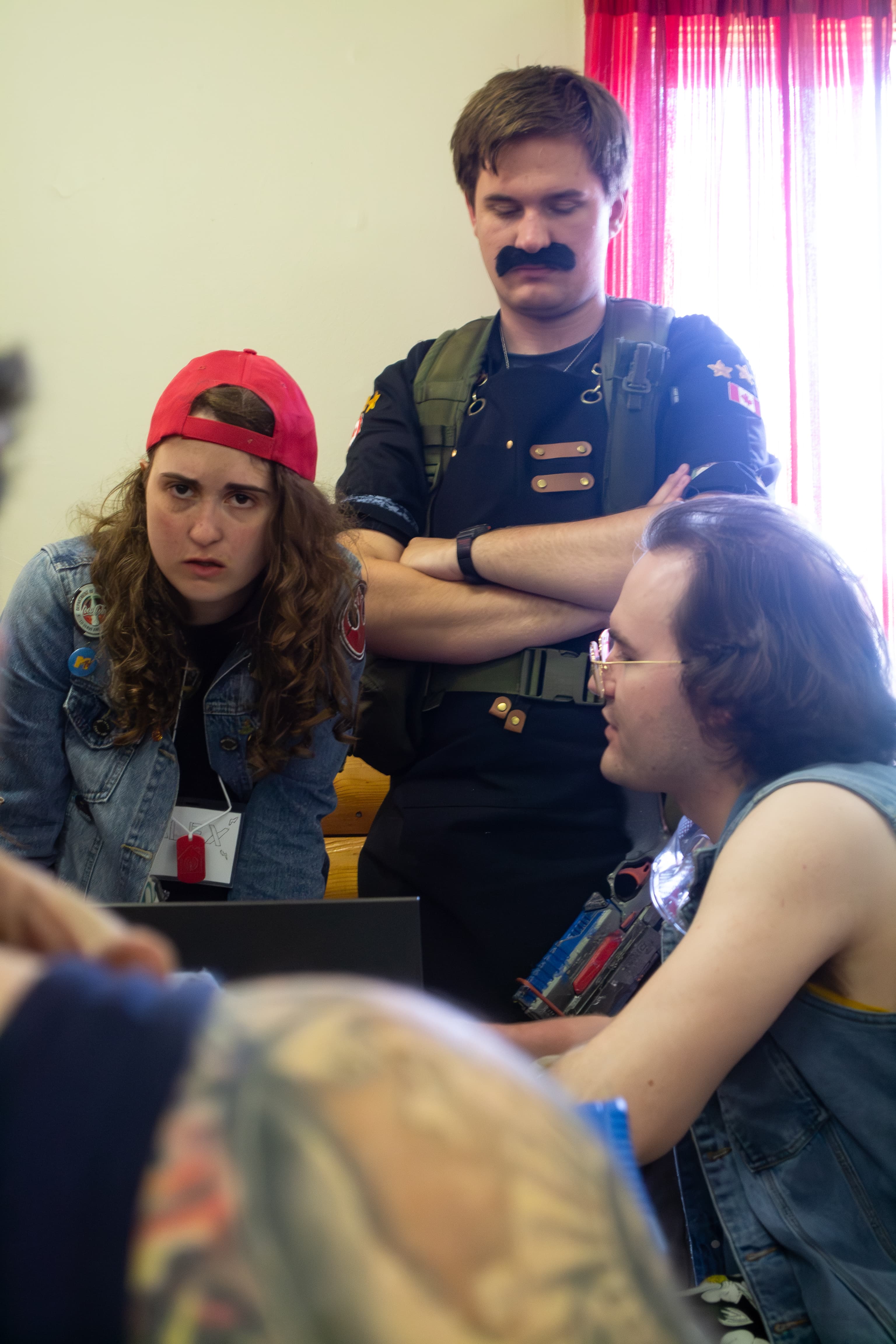 Multiple people wearing post-apocalyptic costumes having an intense discussion. One person has an angry expression on their face while another has their arms crossed and eyes closed.