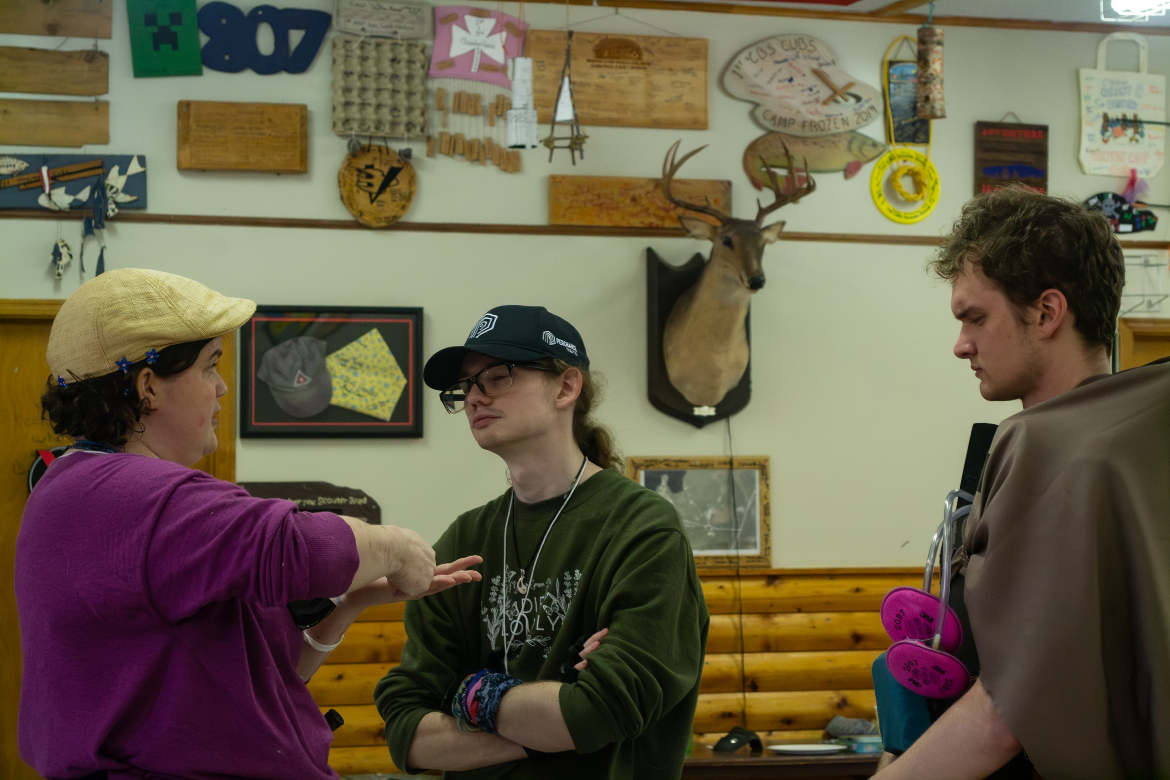 Two people wearing post-apocalyptic costumes are squinting their eyes as they listen to a third person explaining something to them.