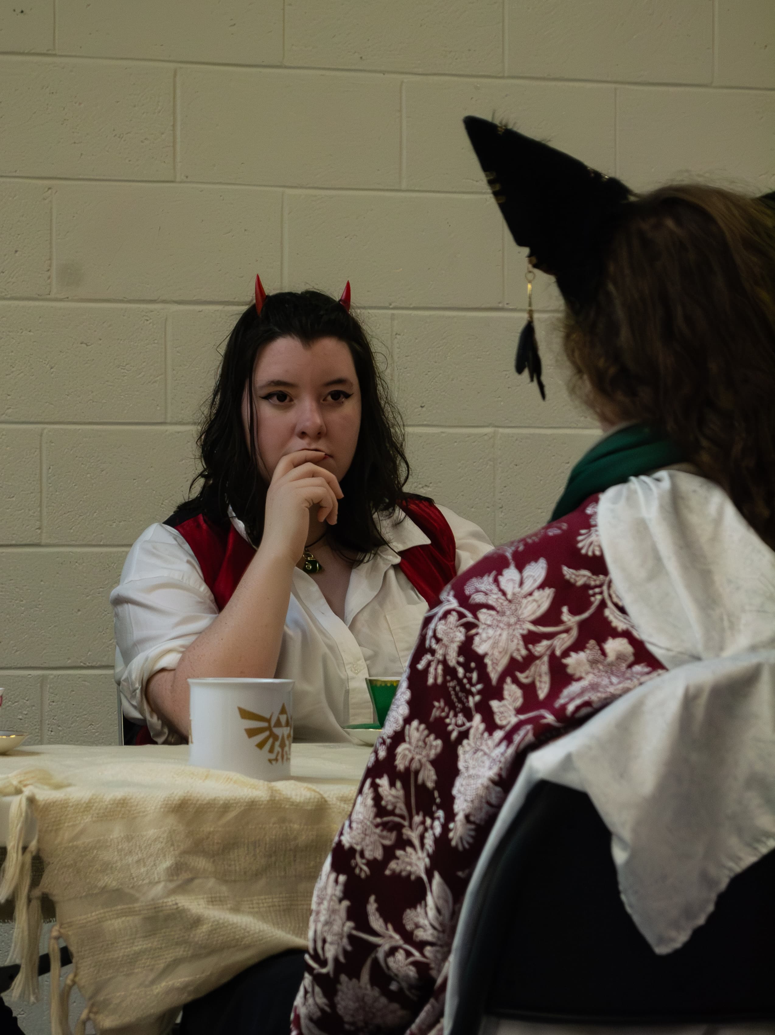 A person wearing a Devil costume stares across a table at a person wearing a kitsune costume.