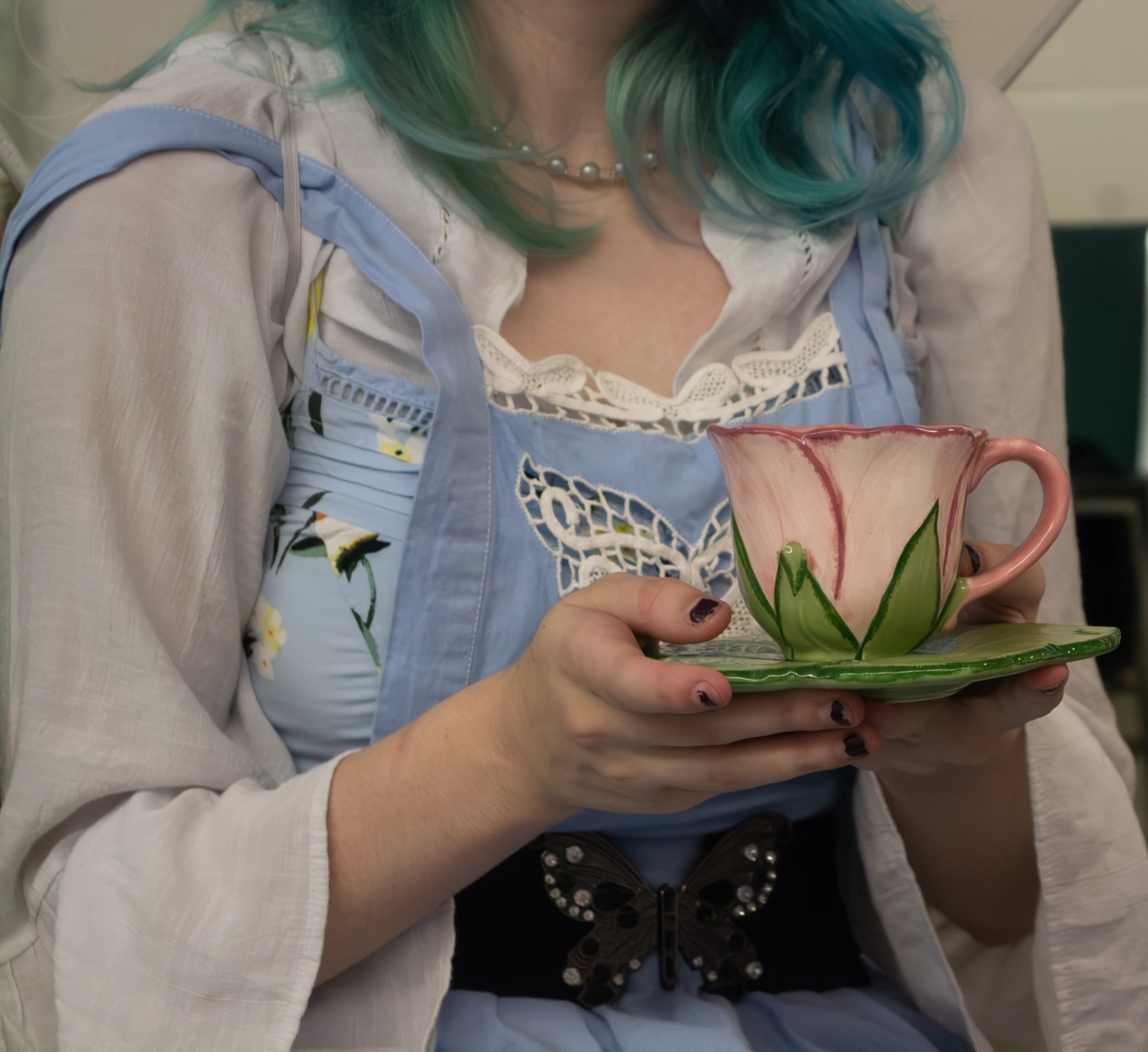 A person wearing a fairy costume holding a floral teacup and saucer.
